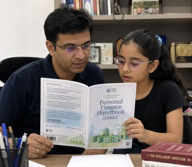 A father and young daughter reading the Personal Finance Handbook together at home, with real parent and student reviews printed on the facing page
